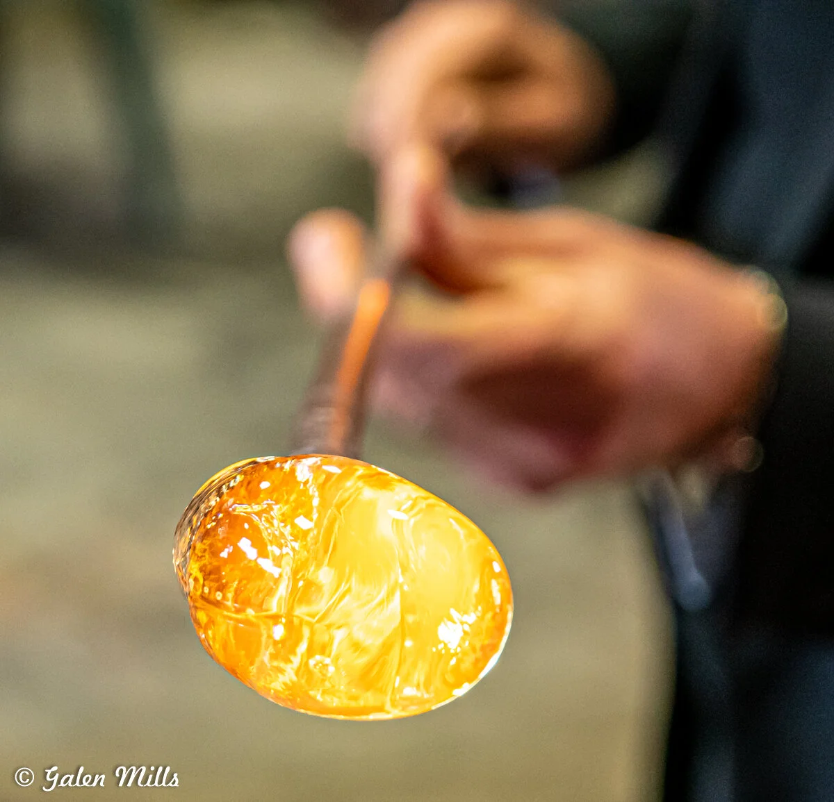 A person holding a molten glass on a rod, showing the glassblowing process.