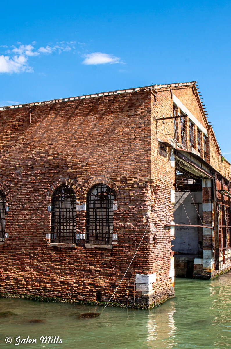 Old brick building by water with barred windows and clear blue sky.