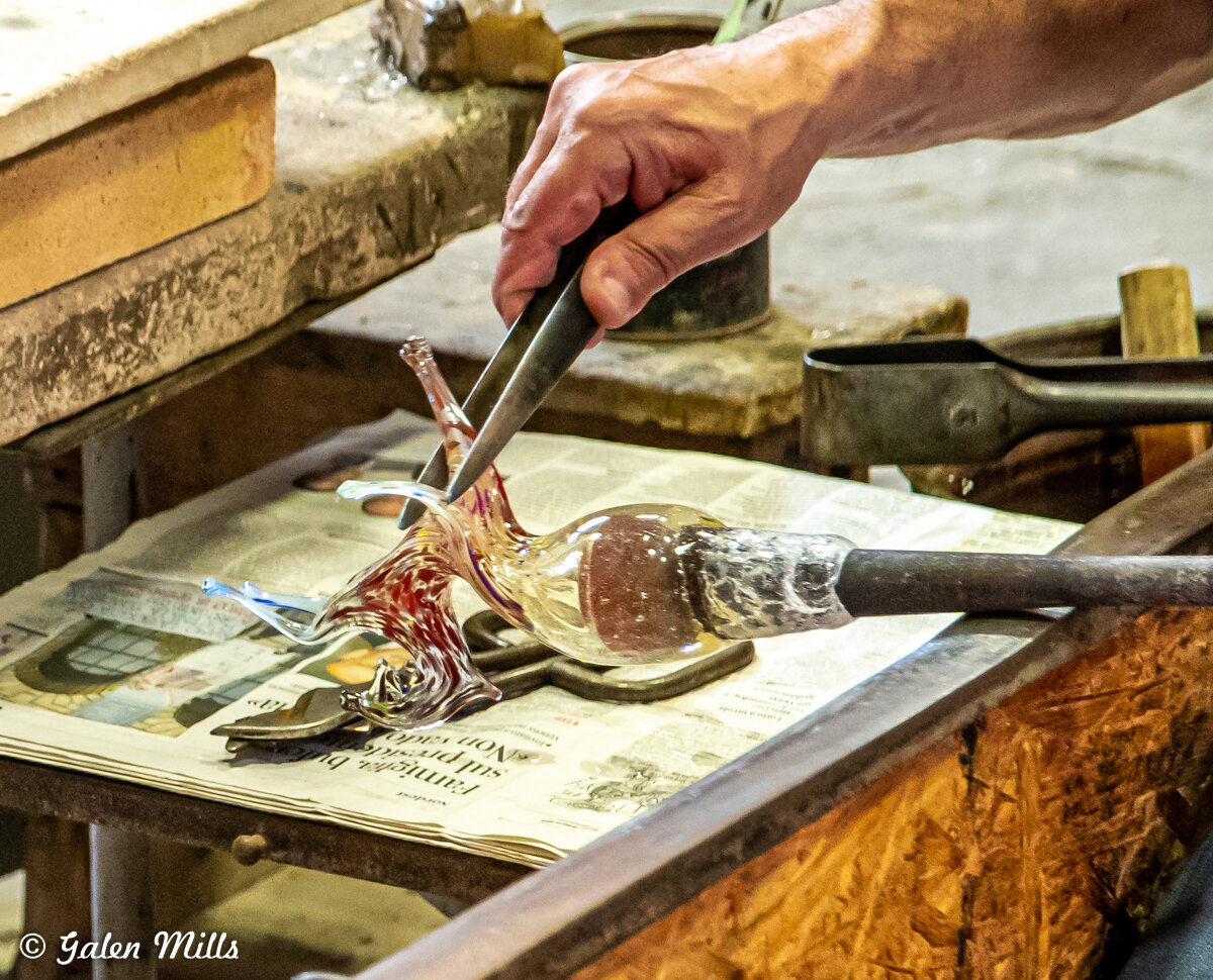 A person shaping a glass sculpture using tools on a workbench.