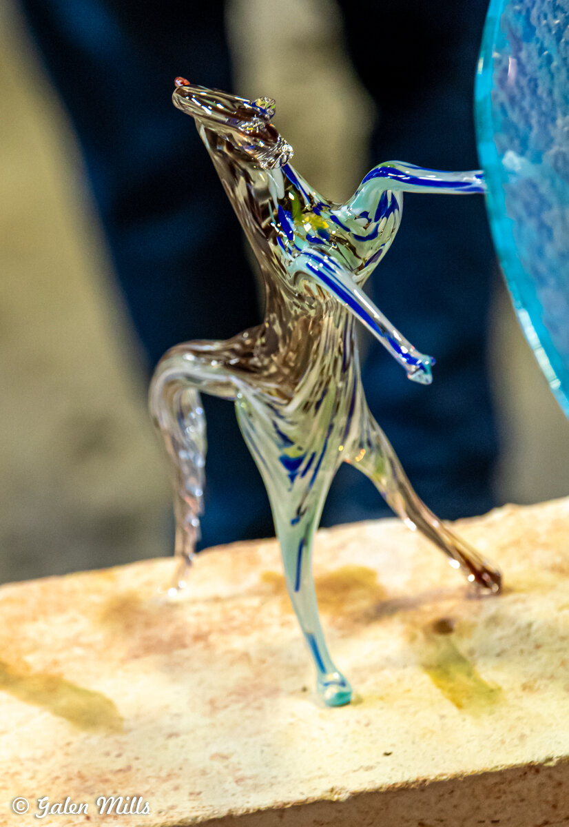 Glass sculpture of a rearing horse with blue accents on a stone surface.