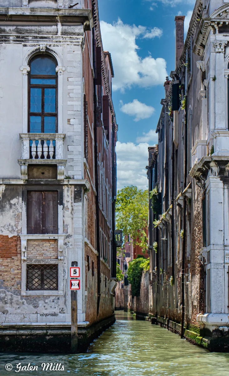 Narrow canal in Venice lined with historic buildings under a blue sky.