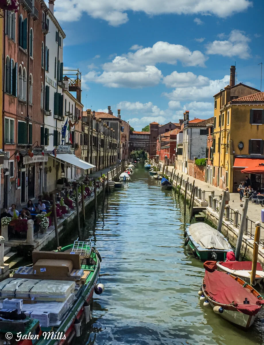 Venetian canal with boats and colorful buildings under blue sky with clouds.