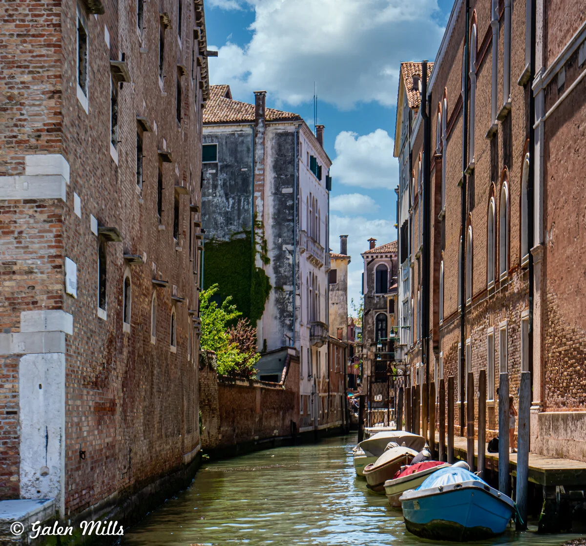 Venetian canal with moored boats and historic buildings on a sunny day.