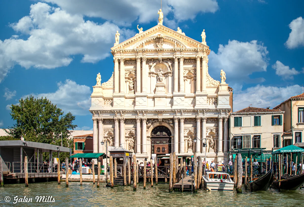 Baroque church facade in Venice with canal and gondolas in foreground.