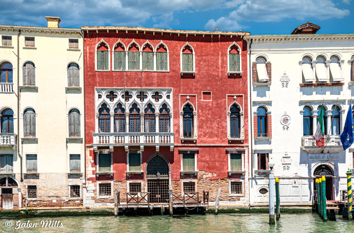 Venetian canal with historic colorful buildings, featuring ornate windows and balconies, under a cloudy sky.