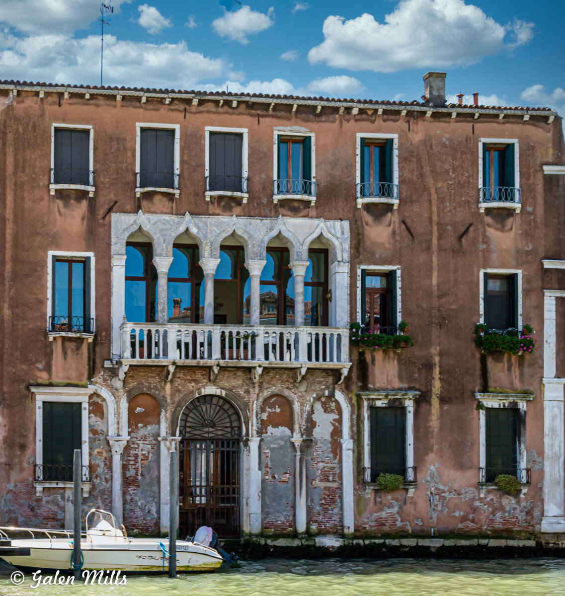 Venetian building by canal with arched windows and balconies, small boat docked.