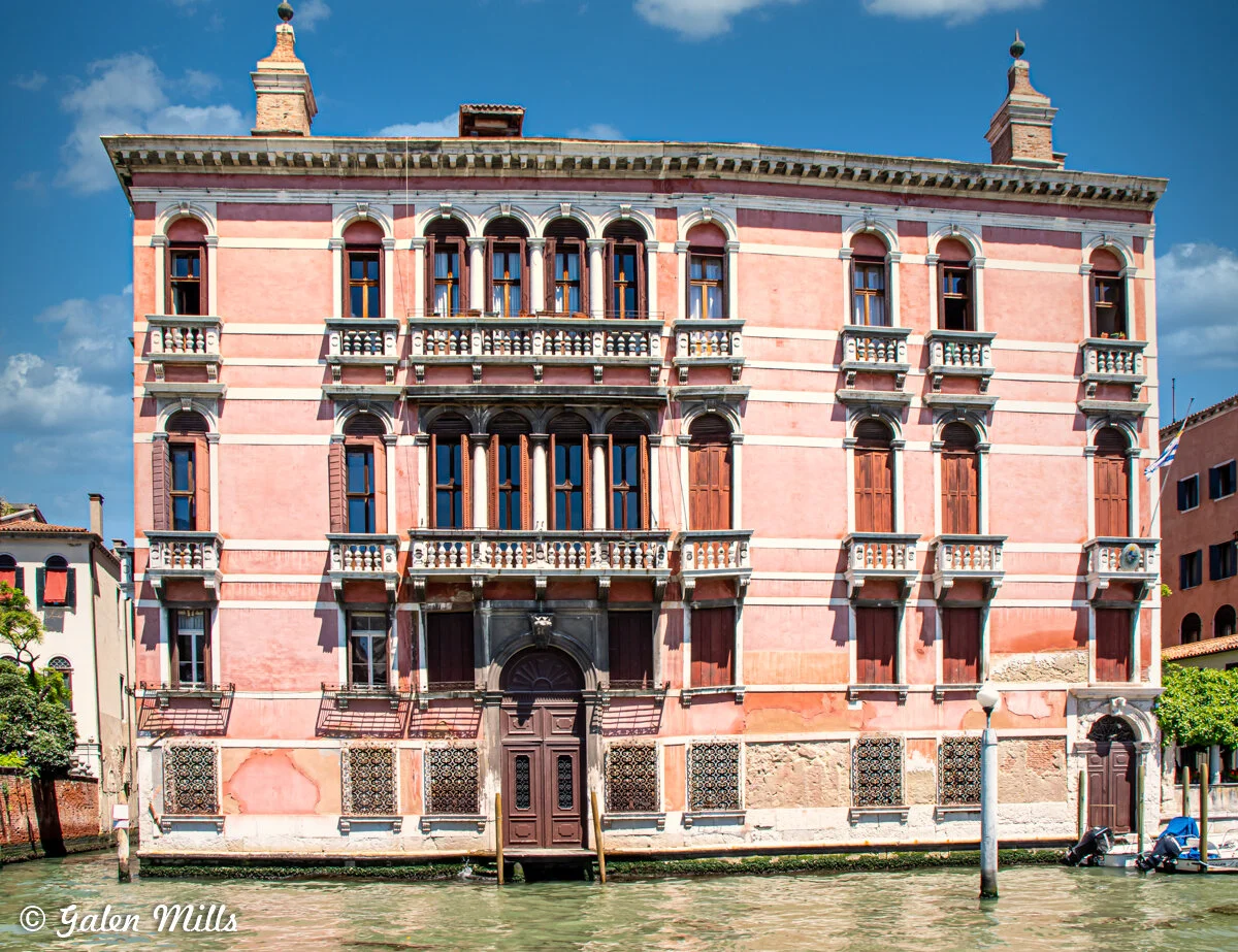 Historic pink building with arched windows and balconies in Venice, Italy, viewed from a canal.