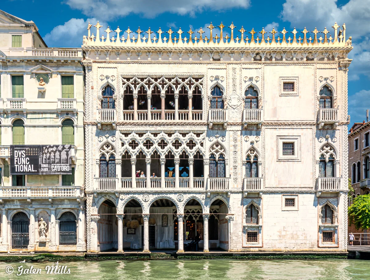 Facade of the Ca' d'Oro, a Gothic-style palace in Venice, Italy, featuring ornate arches, decorative windows, and intricate stonework along a canal.