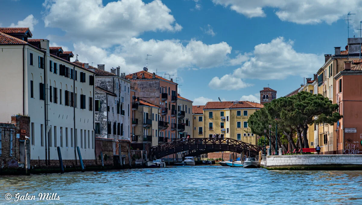 Venetian canal with colorful buildings, a wooden bridge, and boats in Venice, Italy.
