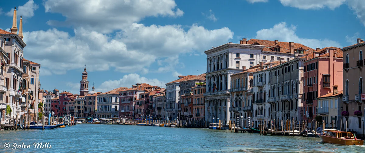 Venice canal with historic buildings, boats, and a bell tower under a cloudy sky.