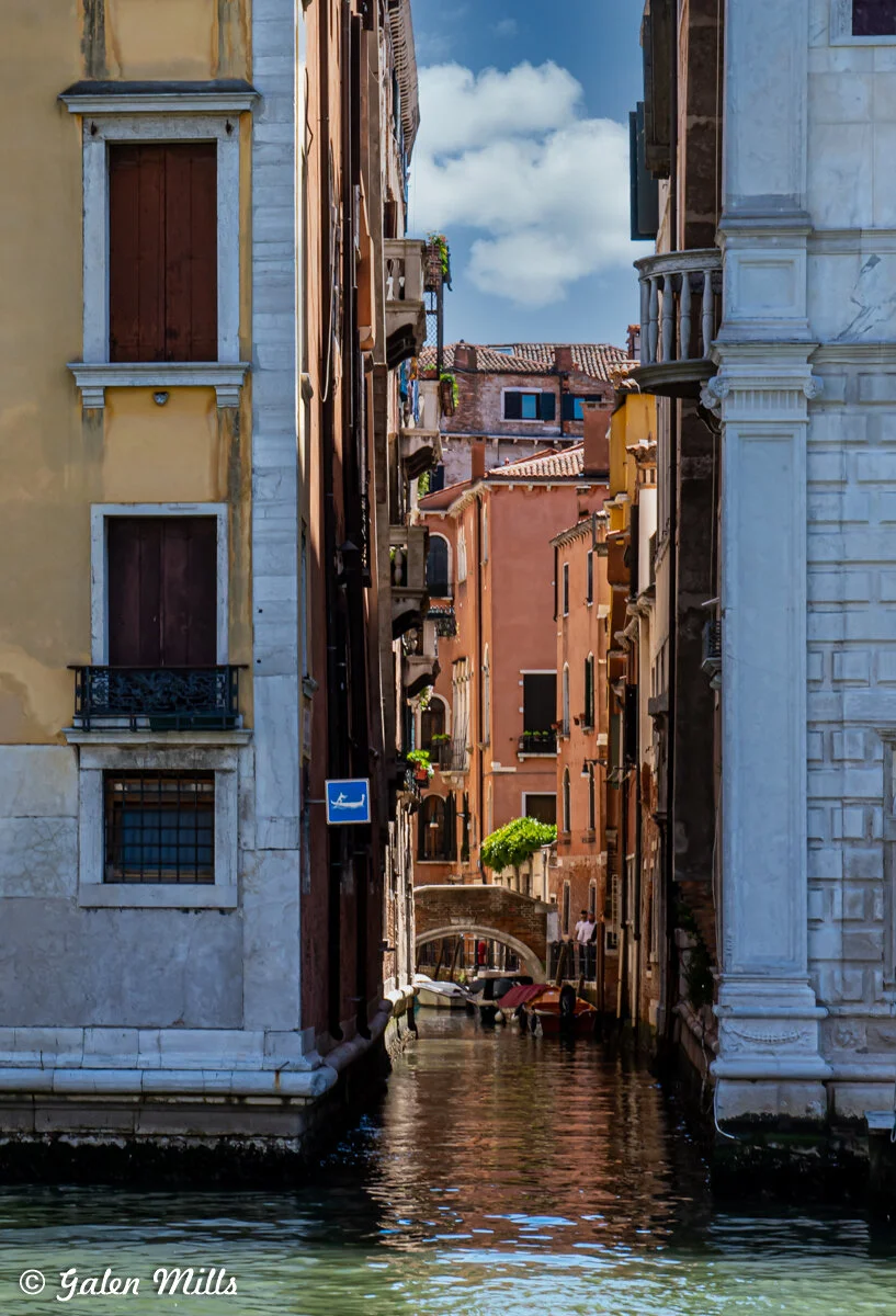 Narrow canal in Venice, Italy, surrounded by colorful historic buildings and small bridge.