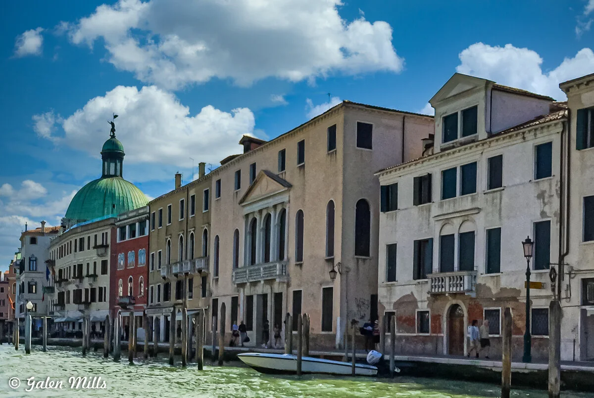Canal in Venice with historic buildings and a green dome, under a blue sky with clouds.