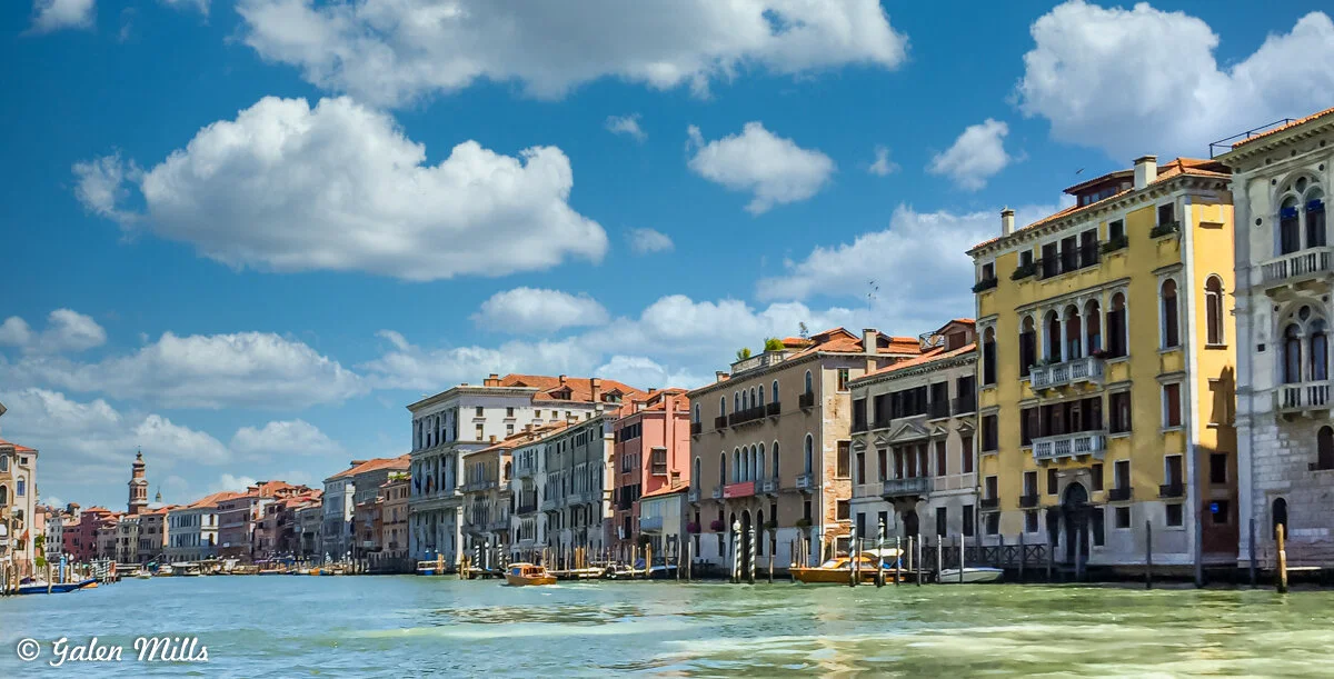 Venetian canal with colorful historic buildings lining the water, blue sky, and fluffy clouds.