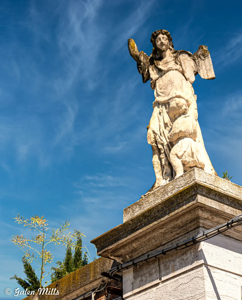 Stone angel statue on a pedestal against a blue sky with wispy clouds.