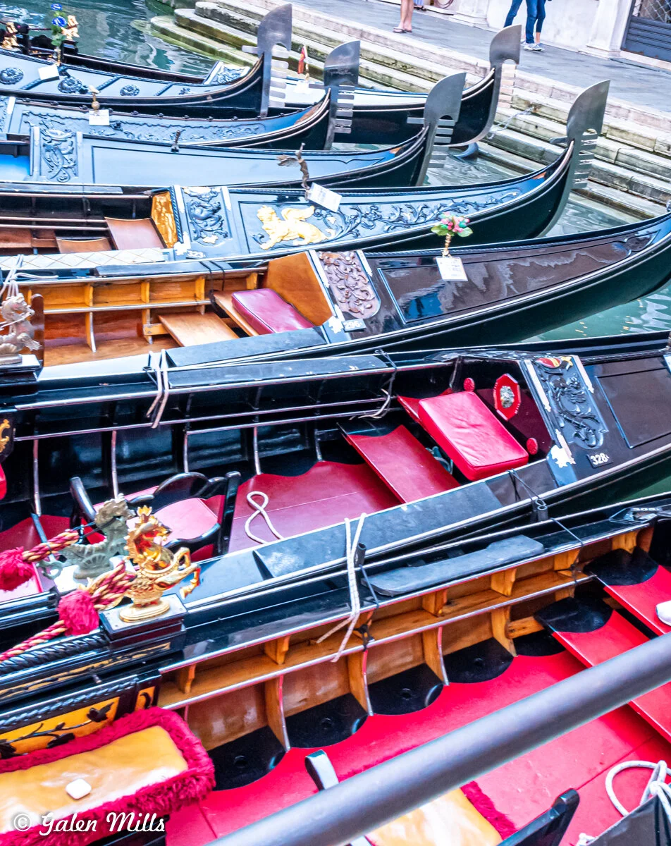 Row of gondolas with ornate decorations and red seats docked at a canal in Venice.