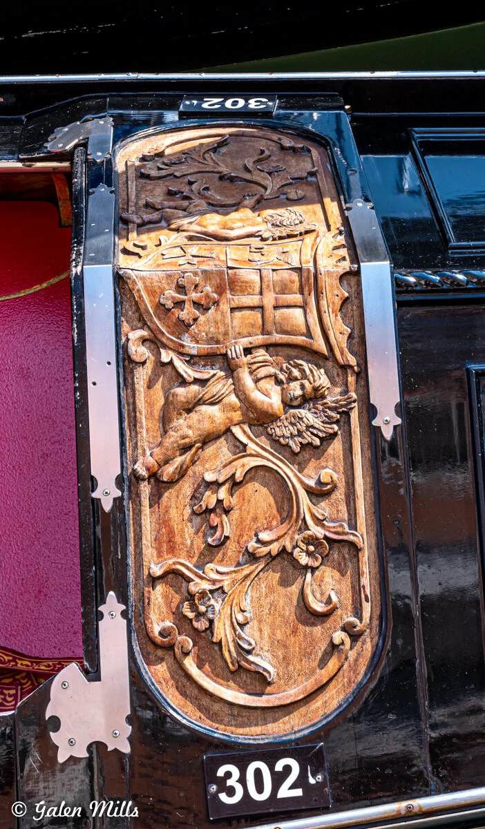 Ornate wood carving on a black gondola in Venice, featuring a cherub and coat of arms.