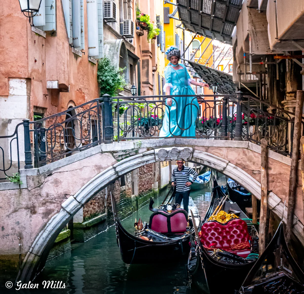 A person in a blue dress walking over a bridge in Venice, Italy. Below is a gondolier navigating a gondola on the canal.