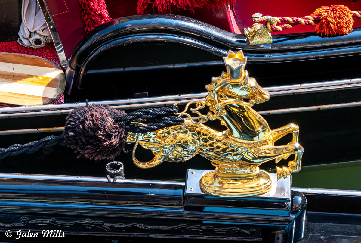 Close-up of a gondola's decorative gold ornament featuring a crowned horse figure, with red and black ropes and boat details.