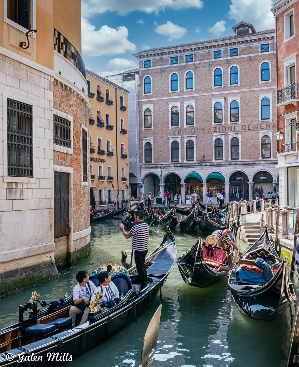 Gondolas on a Venice canal with people, surrounded by historic buildings.