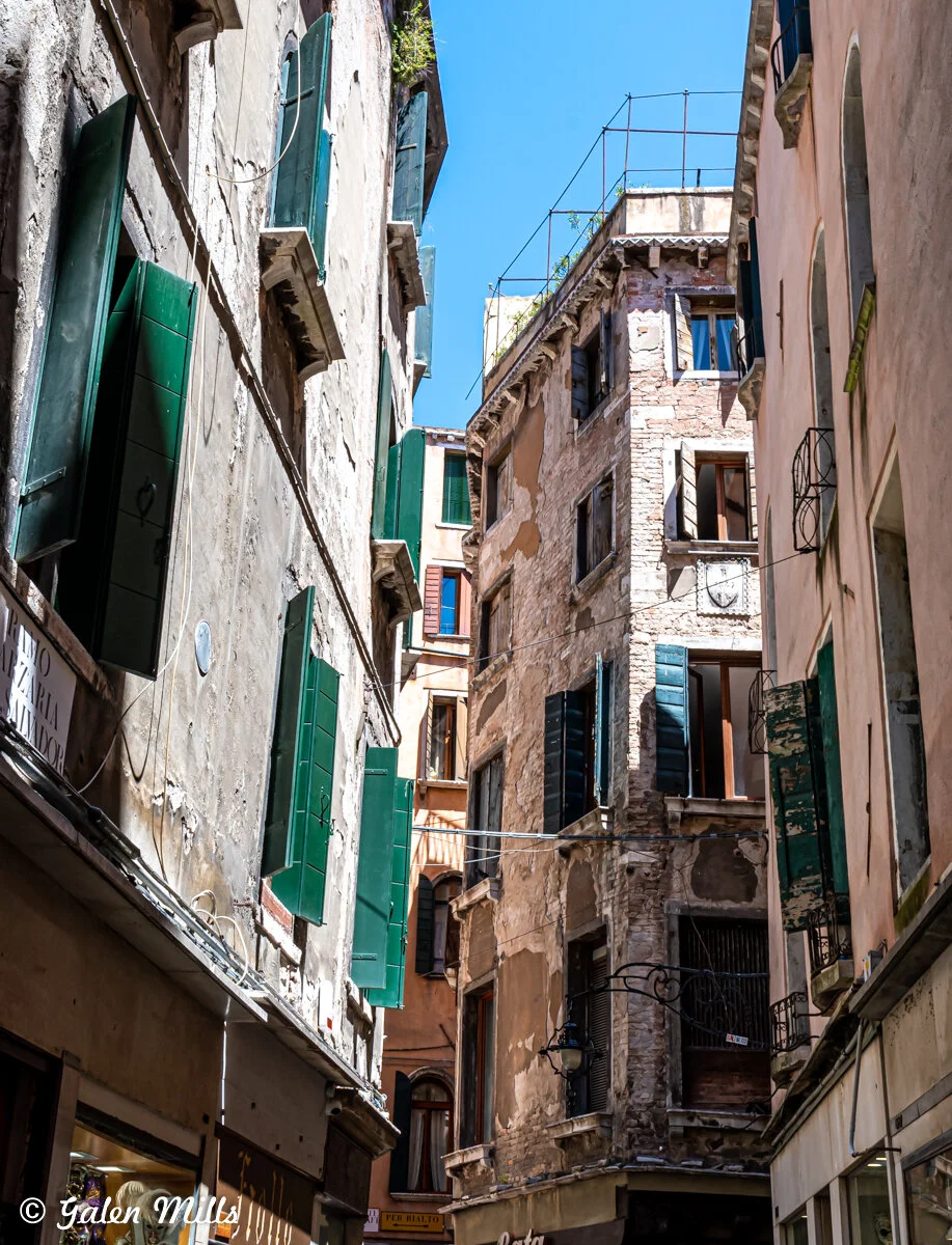 Narrow European street with old buildings, green shutters, blue sky.