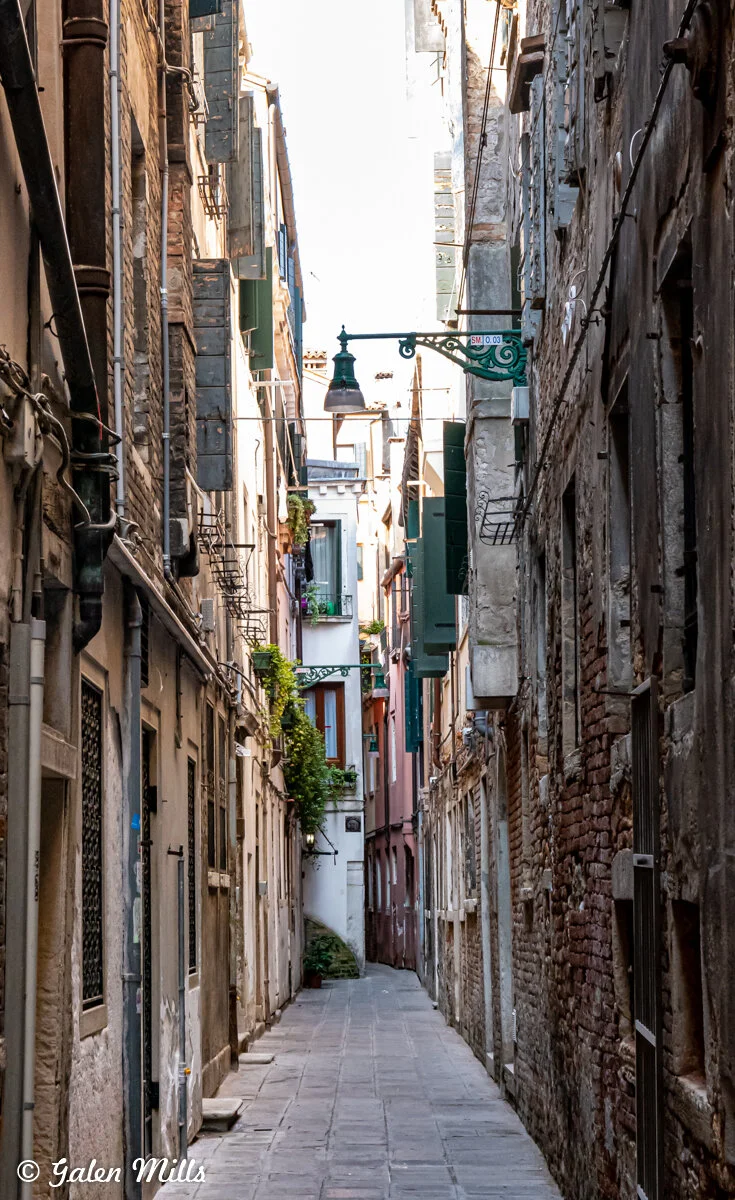 Narrow European alleyway lined with old buildings and shutters.