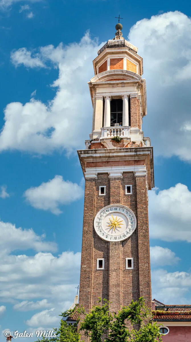 Clock tower with ornate circular clock face against blue sky with clouds.