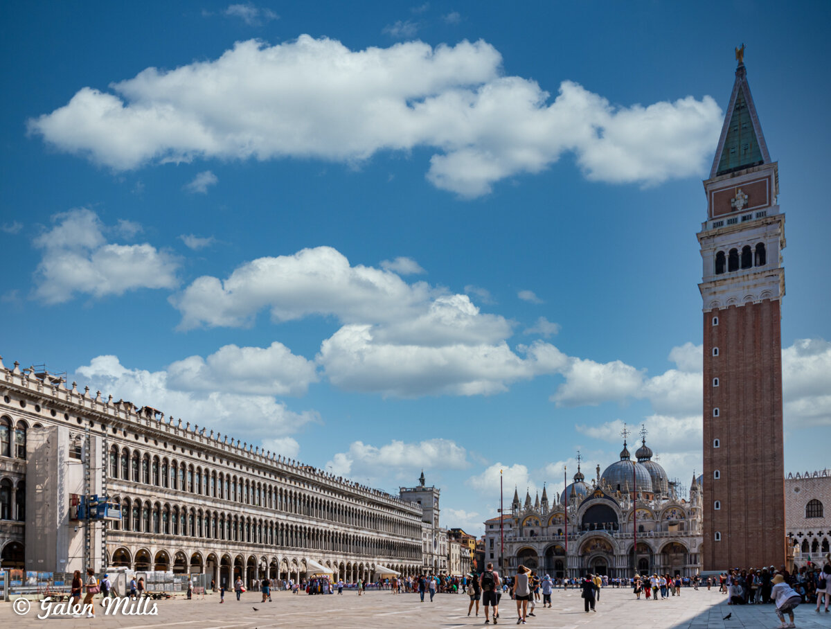 St. Mark's Square in Venice, Italy with St. Mark's Basilica and Campanile tower under a blue sky with clouds.