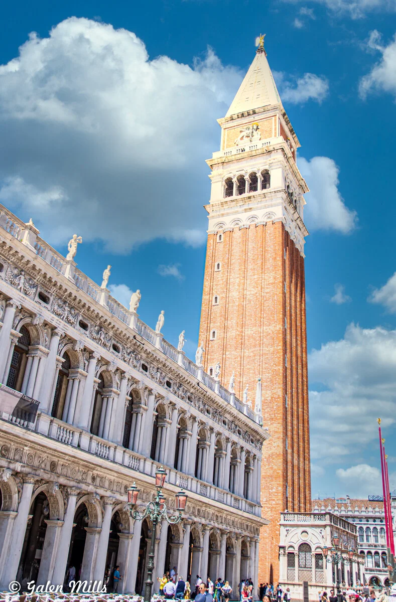 St. Mark's Campanile and adjacent building in Venice, Italy under a blue sky with clouds.