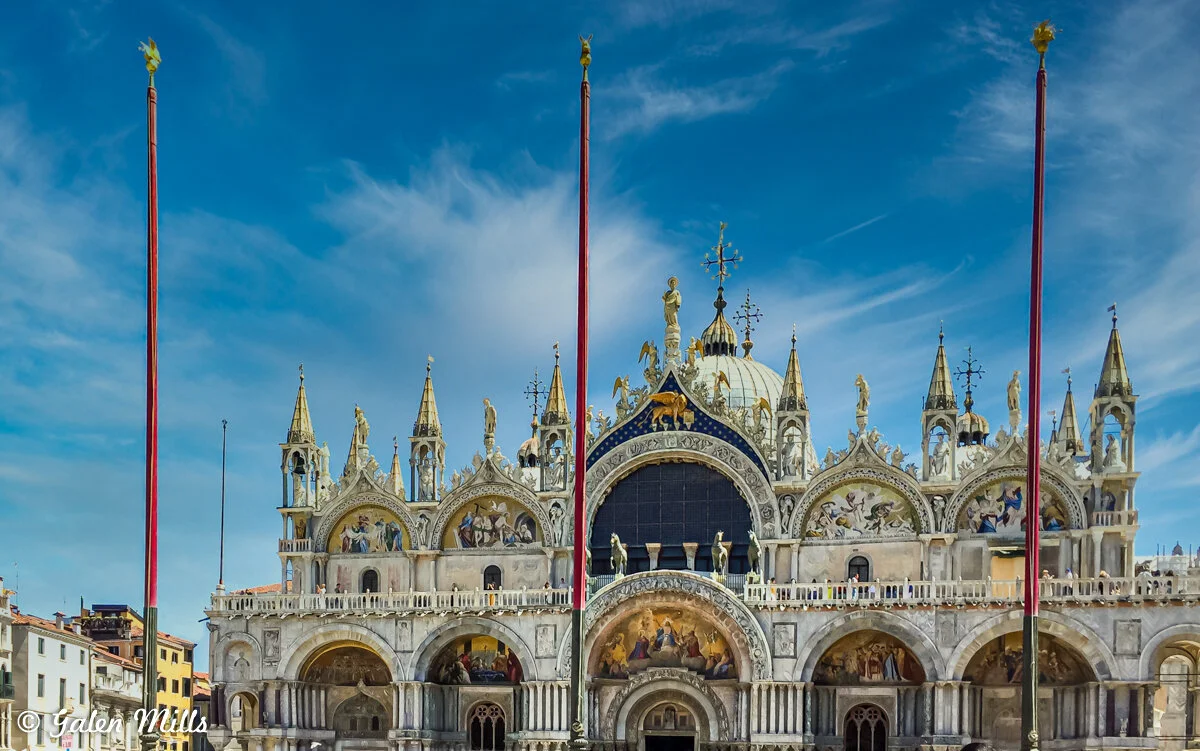 St. Mark's Basilica in Venice with blue sky background and flagpoles in front.