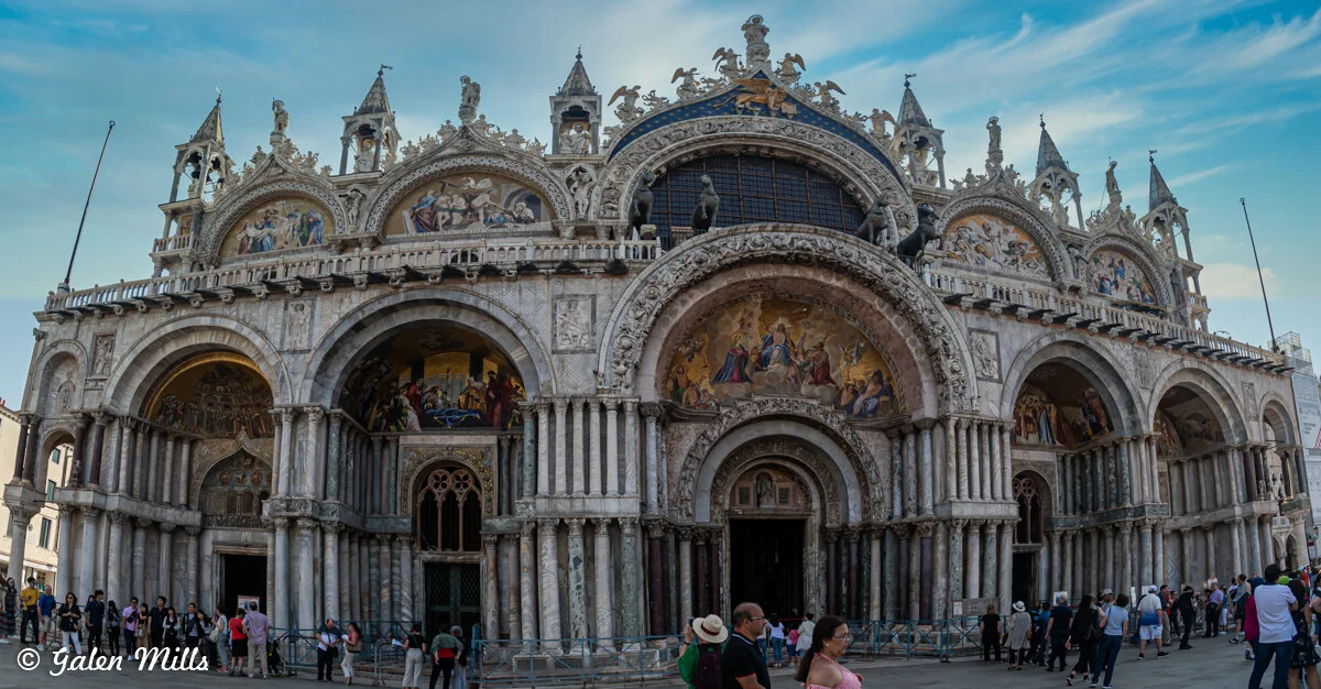 Facade of St. Mark's Basilica in Venice, Italy, featuring intricate mosaics and sculptures with tourists in the foreground.