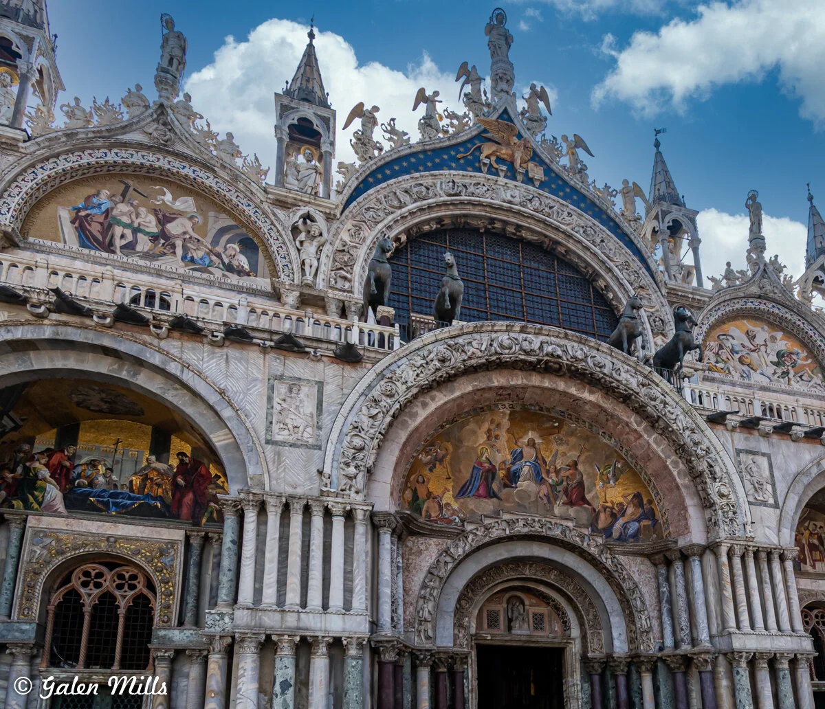 Exterior of St. Mark's Basilica in Venice, Italy, featuring intricate mosaics, sculptures, and architectural details under a blue sky.