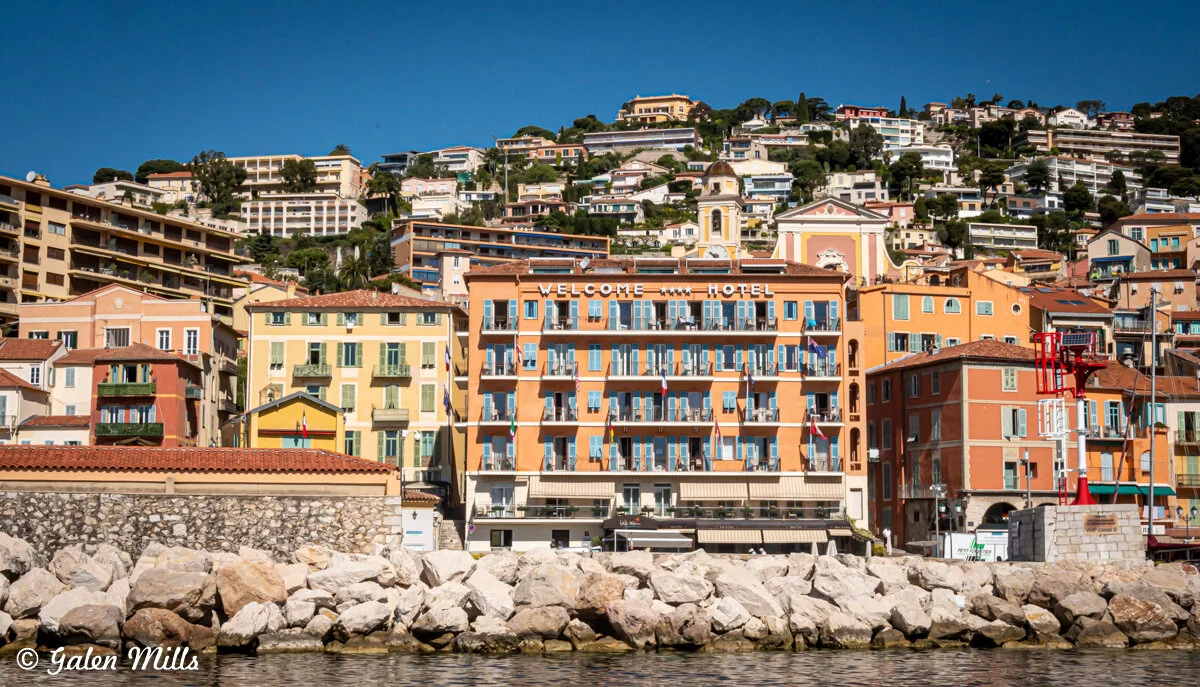 Seaside hotel with colorful buildings in a coastal, hillside village under a clear blue sky.
