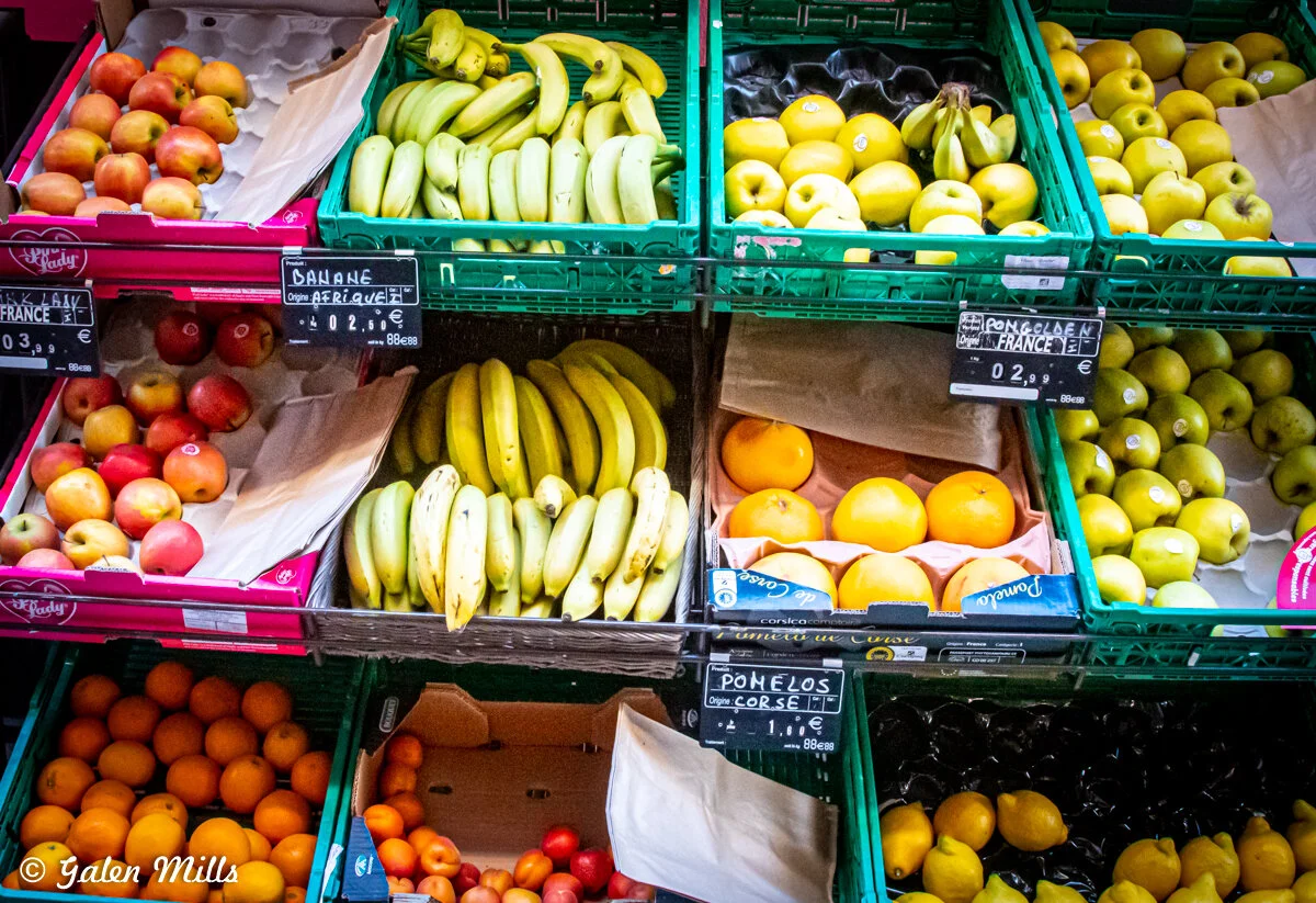Assorted fresh fruits on display at a market, including bananas, apples, oranges, and pomelos, with price signs in euros.