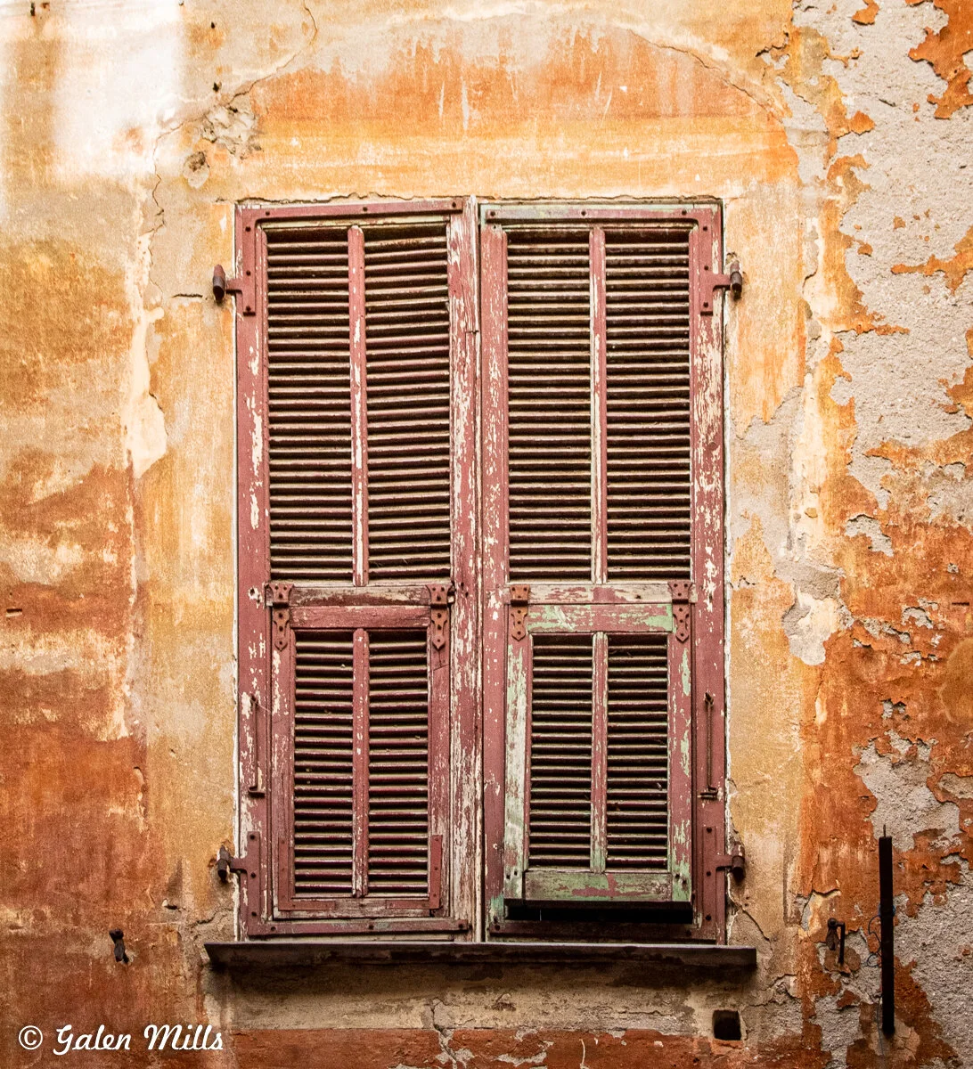 Old weathered shutters on a textured, peeling wall.