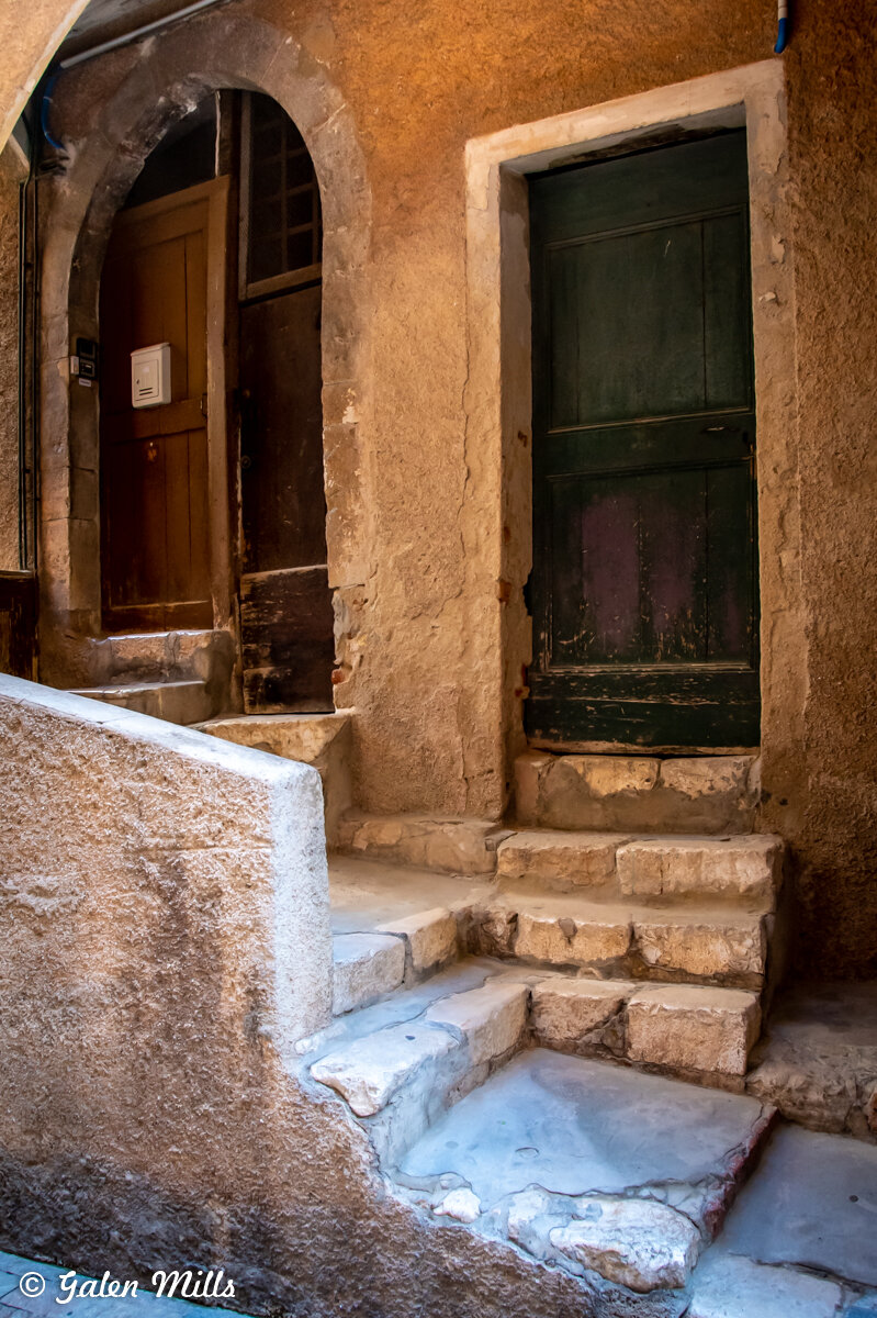 Old stone staircase leading to two weathered wooden doors set in textured walls.