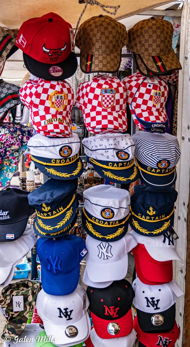Display of assorted hats including sports team caps, Croatian themed caps, and captain hats in various colors and designs.