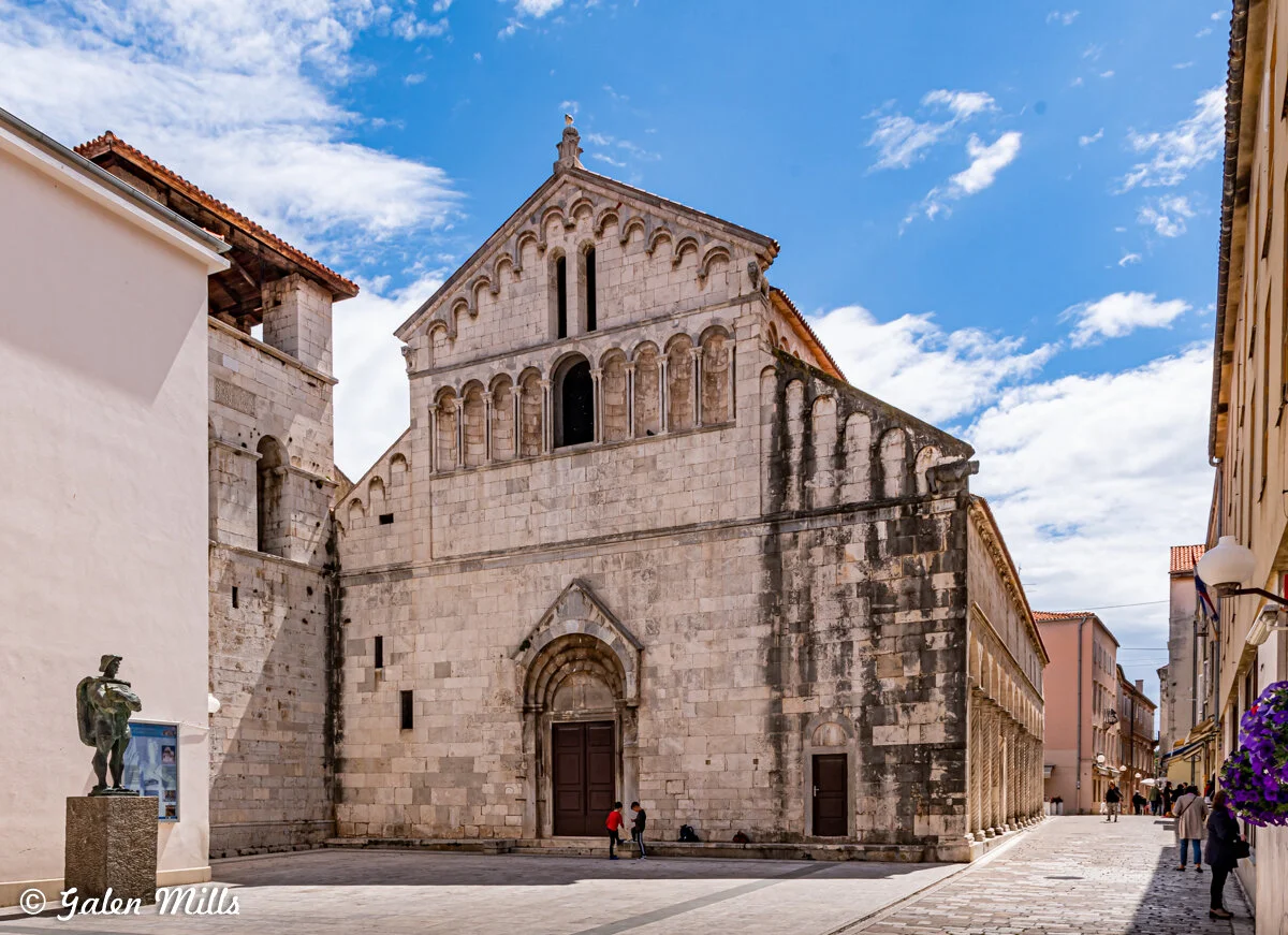 Historic stone church facade with intricate architecture in a European town square, blue sky background.