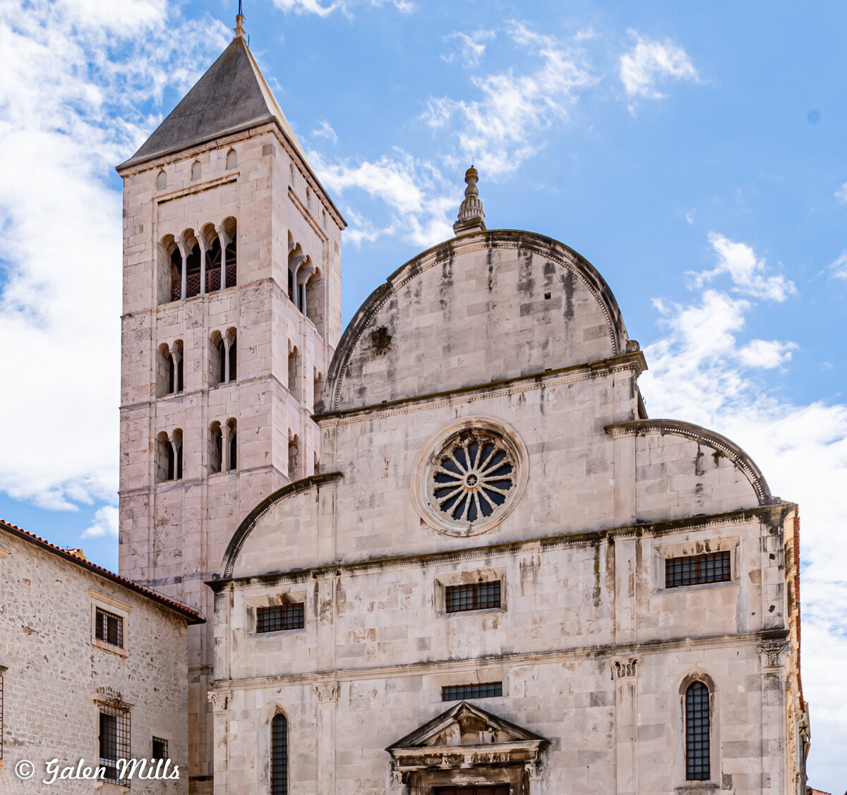 Historic stone church with a tall bell tower and decorative facade against a blue sky.