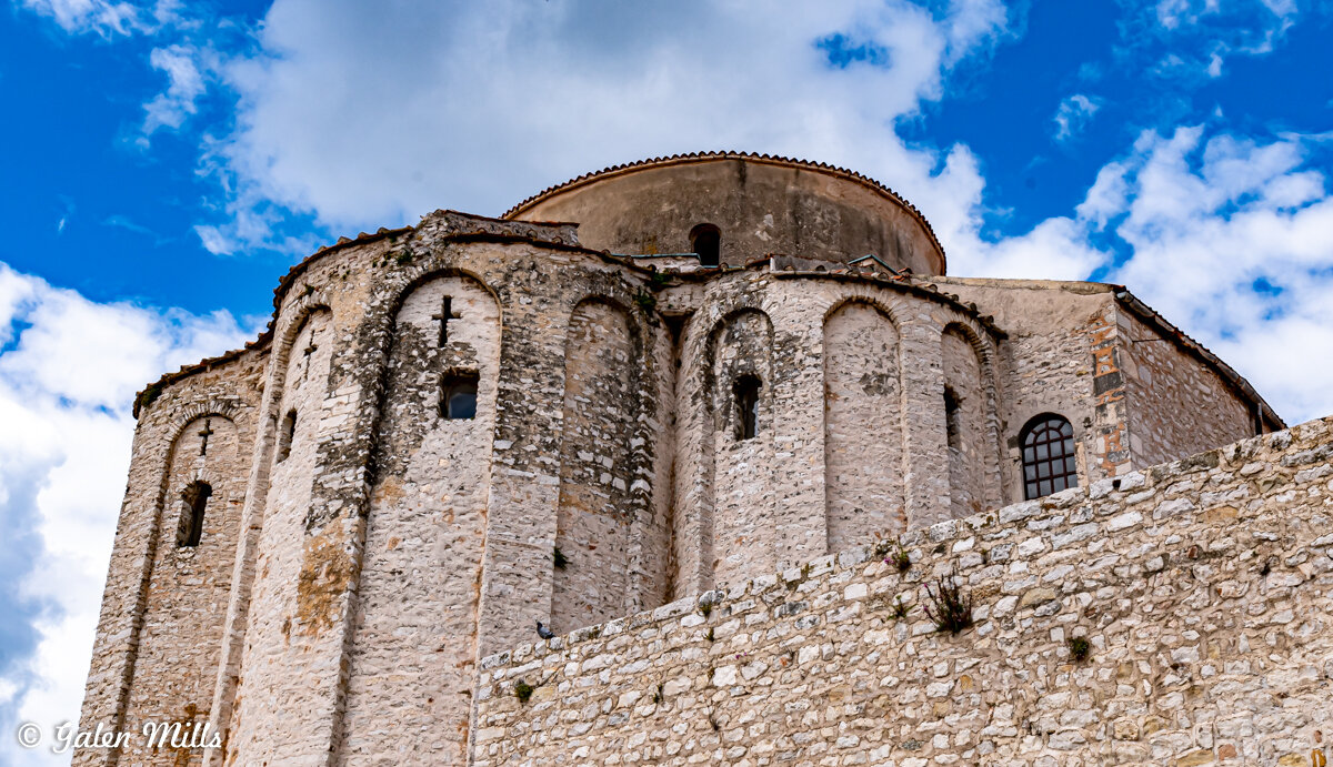 Ancient stone church with arched windows under a cloudy blue sky.