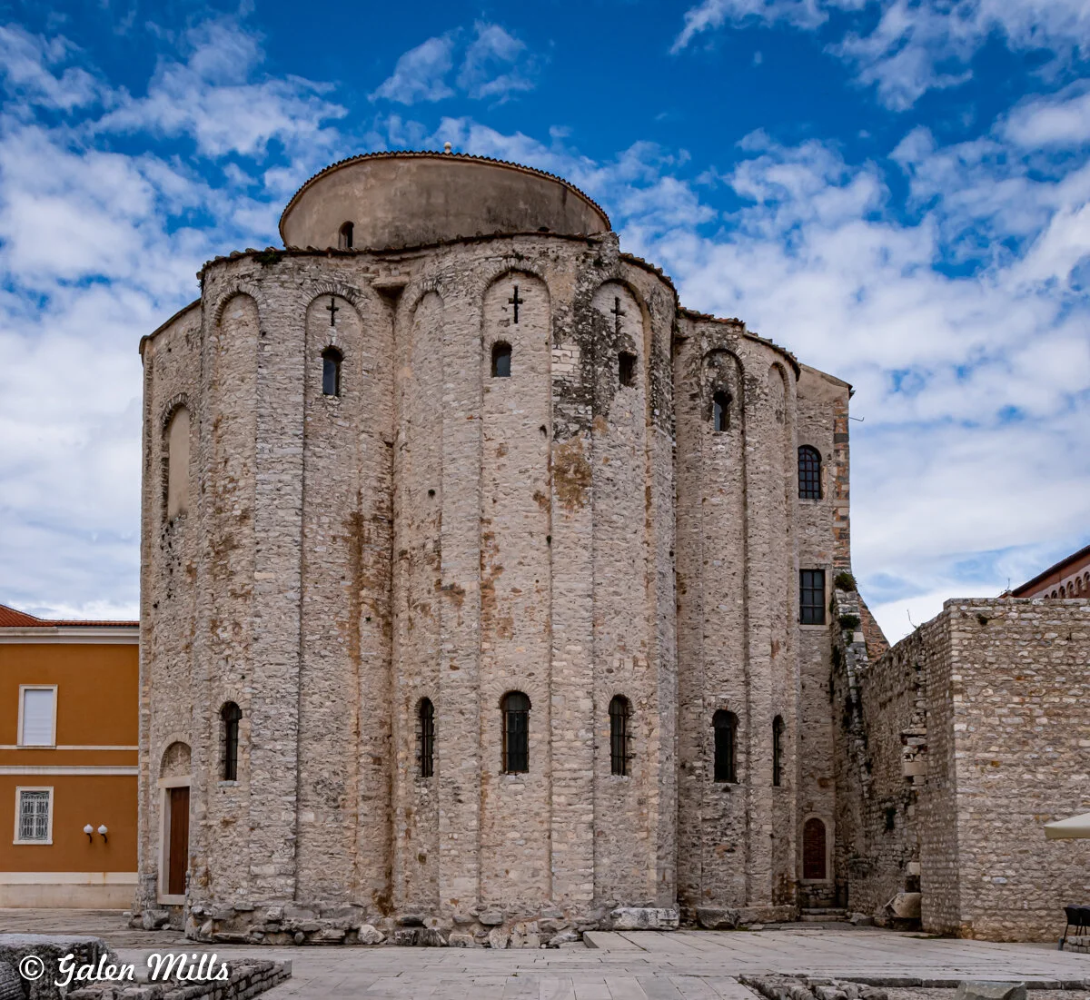 Ancient stone building with arched windows against a cloudy sky.