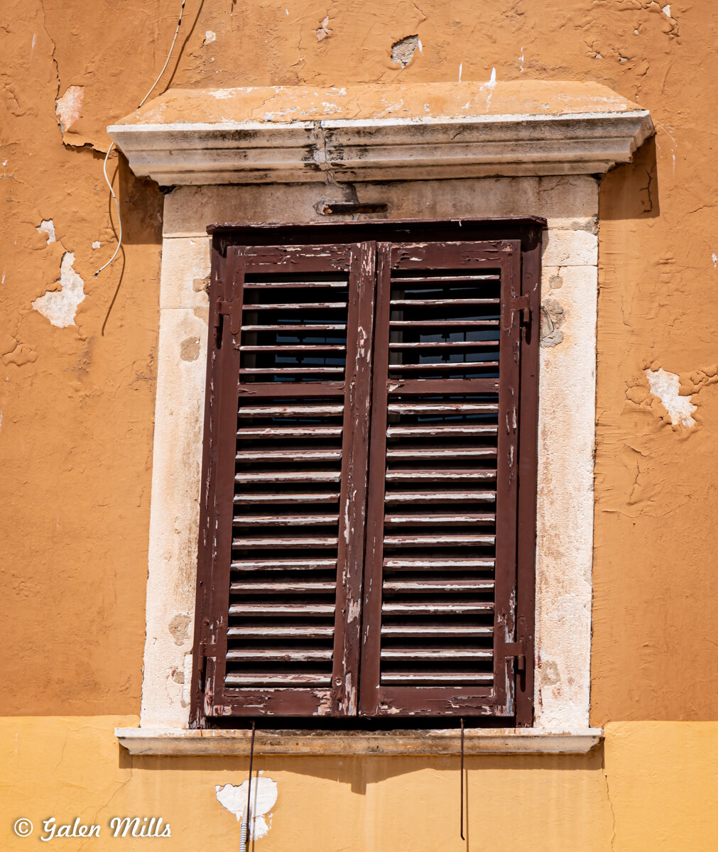 Weathered wooden shutters on a rustic, textured yellow wall with peeling paint.