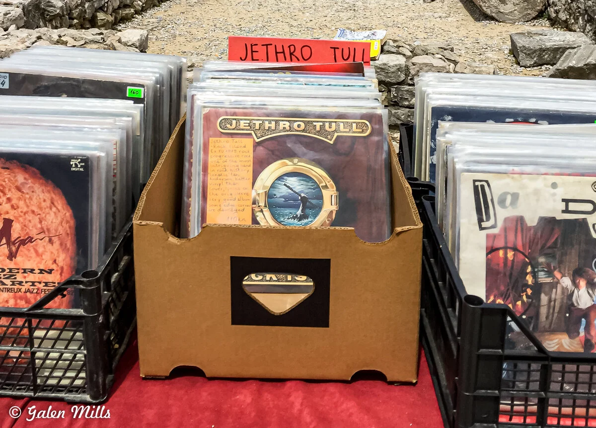 Vinyl records in a crate labeled 'Jethro Tull' displayed at an outdoor market or store.