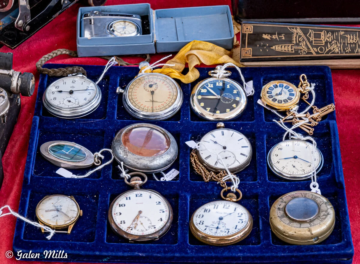 A collection of vintage pocket watches displayed in a blue velvet tray, featuring various designs and styles, with some watches showing chains attached.
