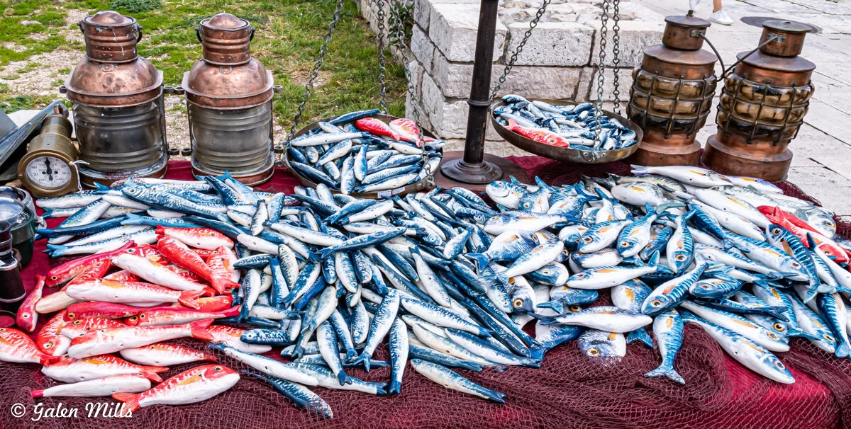 Display of colorful toy fish on a table with brass lanterns and a vintage scale outdoors.