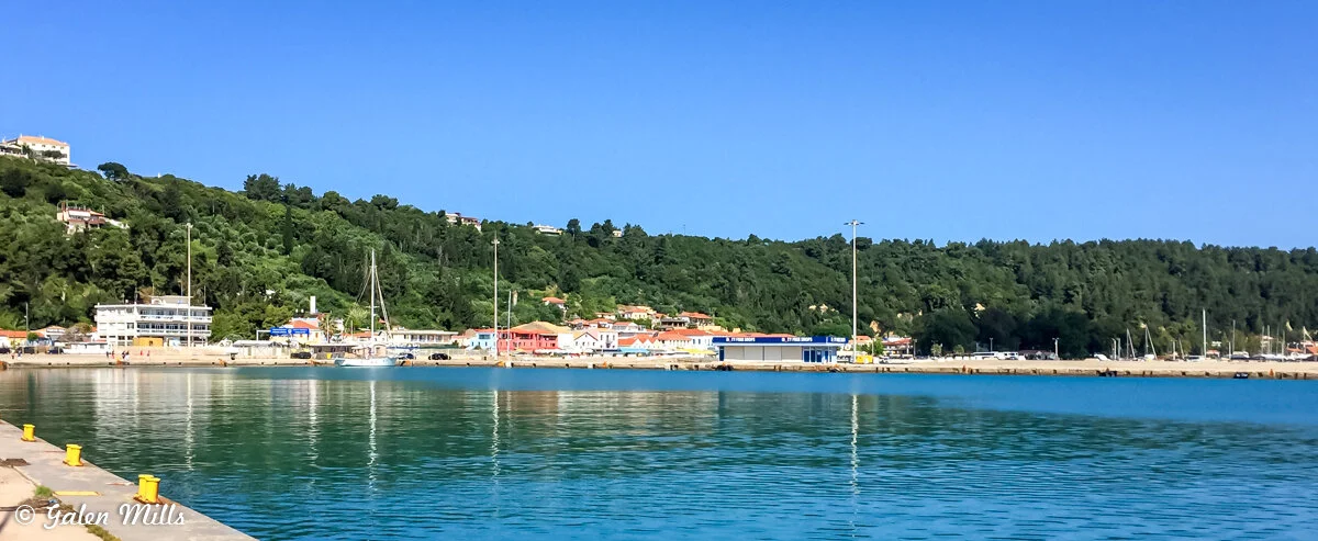 Harbor with boats, green hillside, and buildings under a clear blue sky