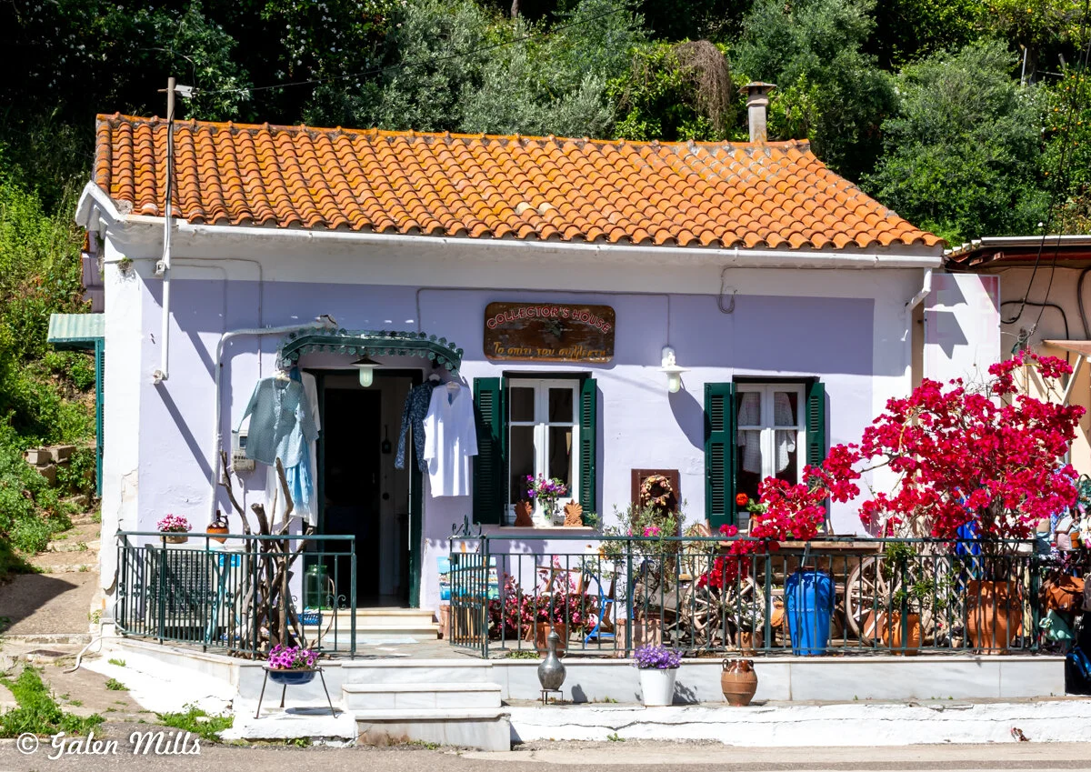 Charming small house with white walls and orange-tiled roof, decorative plants, and flowers outside.