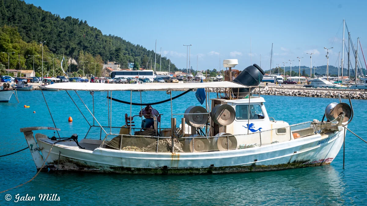 Fishing boat docked in a marina with nets and equipment, surrounded by water and distant trees.