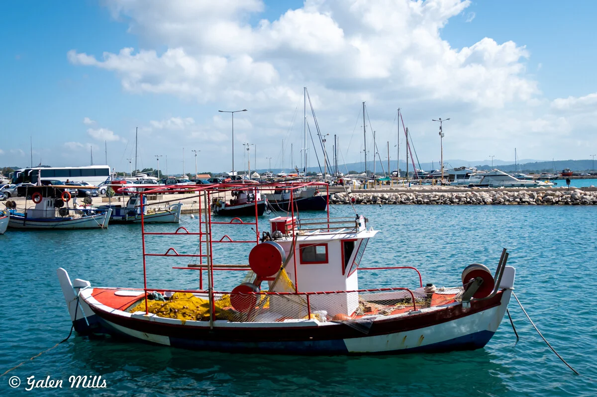 Fishing boat docked in a marina with other sailboats and yachts, clear blue sky, and calm water.