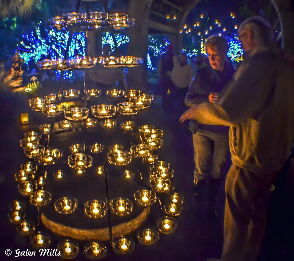 Candle-lit display with hanging lights in a dim outdoor setting, with two people observing.