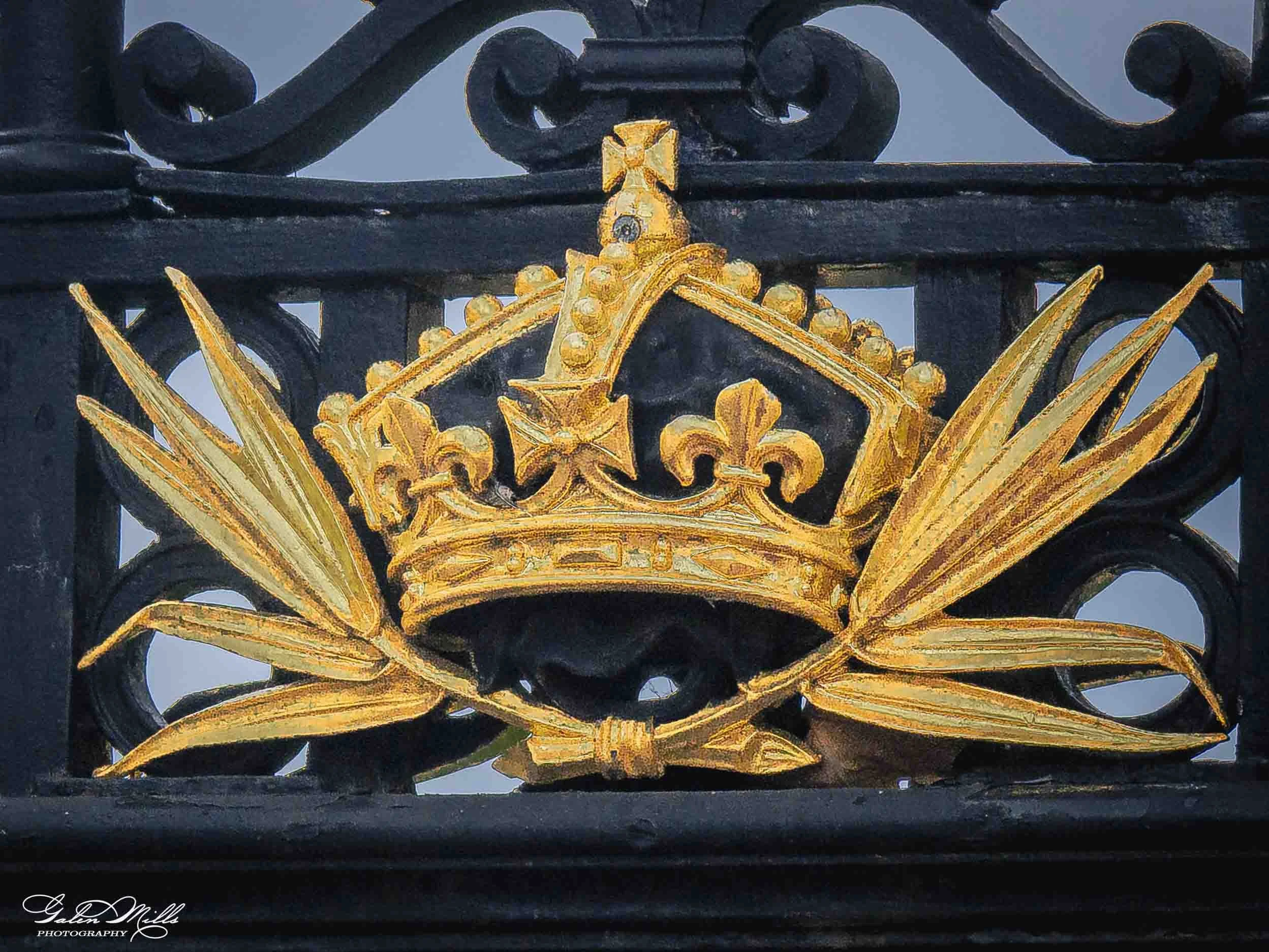 Close-up of a black wrought iron fence with ornate gold accents, including a crown-shaped decoration in the center.